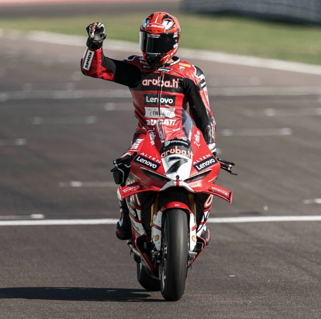 Fahrer des Teams Aruba.it Racing – Ducati mit der Startnummer 7 reckt auf der Strecke auf der Panigale V4 die Faust, mit dem simyousoon-Logo auf der Verkleidung